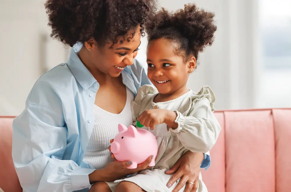 A mom and daughter put money in a piggy bank.