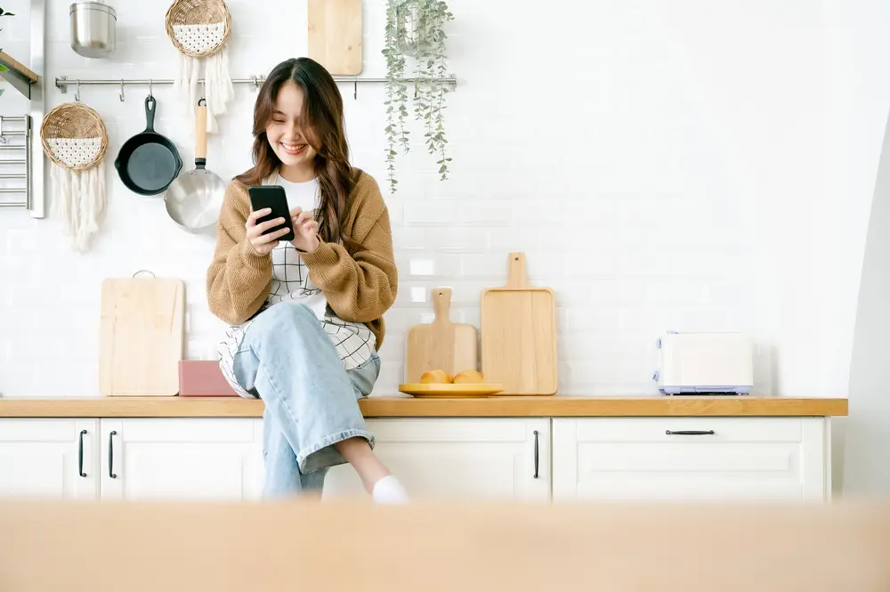 A woman sitting on her kitchen counter with her cell phone.