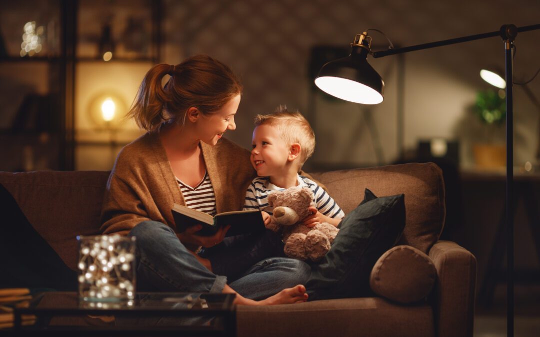 A mother and child sitting on a couch reading a book.